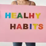 A woman holds a pink poster with colorful letters spelling 'HEALTHY HABITS'.