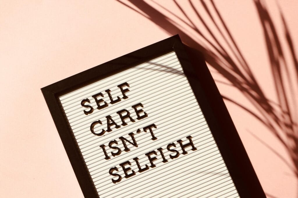 Affiliate Disclosure: Letter board displaying 'Self Care Isn't Selfish' with artistic shadow on pink background.