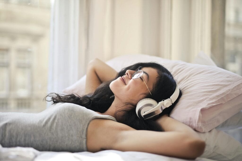 Stress Management Techniques to Improve Your Life A woman with headphones lying on a bed, enjoying music in a relaxed, cozy setting.